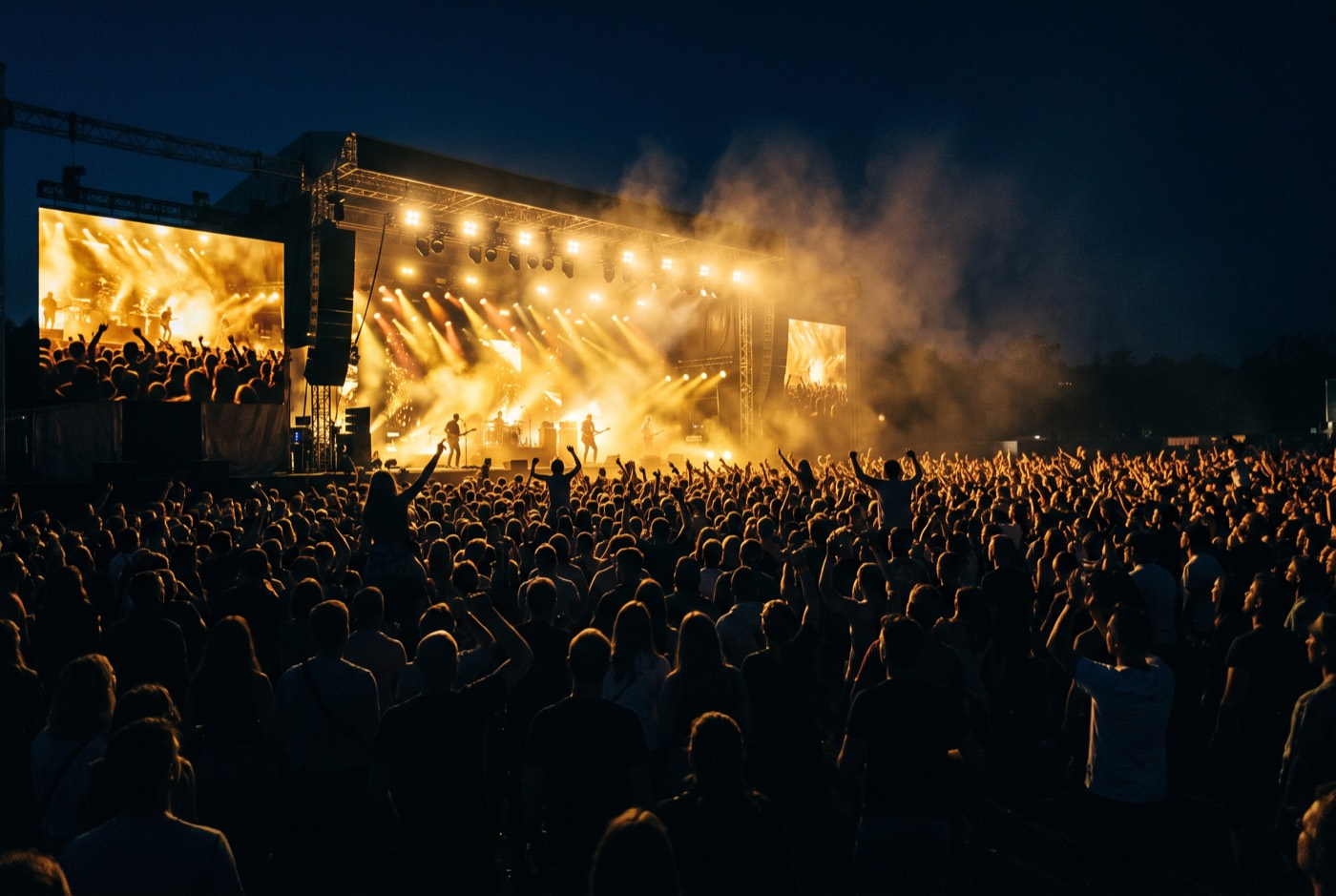 Crowd in silhouette facing a stage lit with golden spotlights